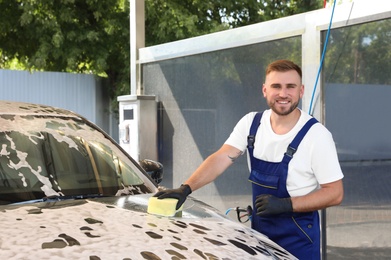 Young worker cleaning automobile with sponge at car wash