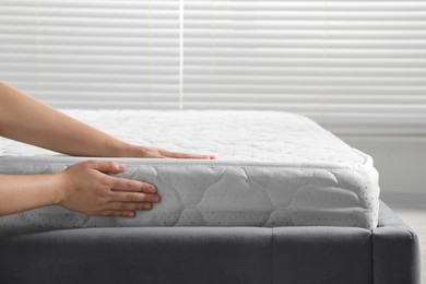 Photo of Woman touching soft light green mattress indoors, closeup