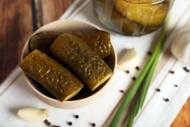 Photo of Bowl with tasty pickled cucumbers and ingredients on wooden table, closeup