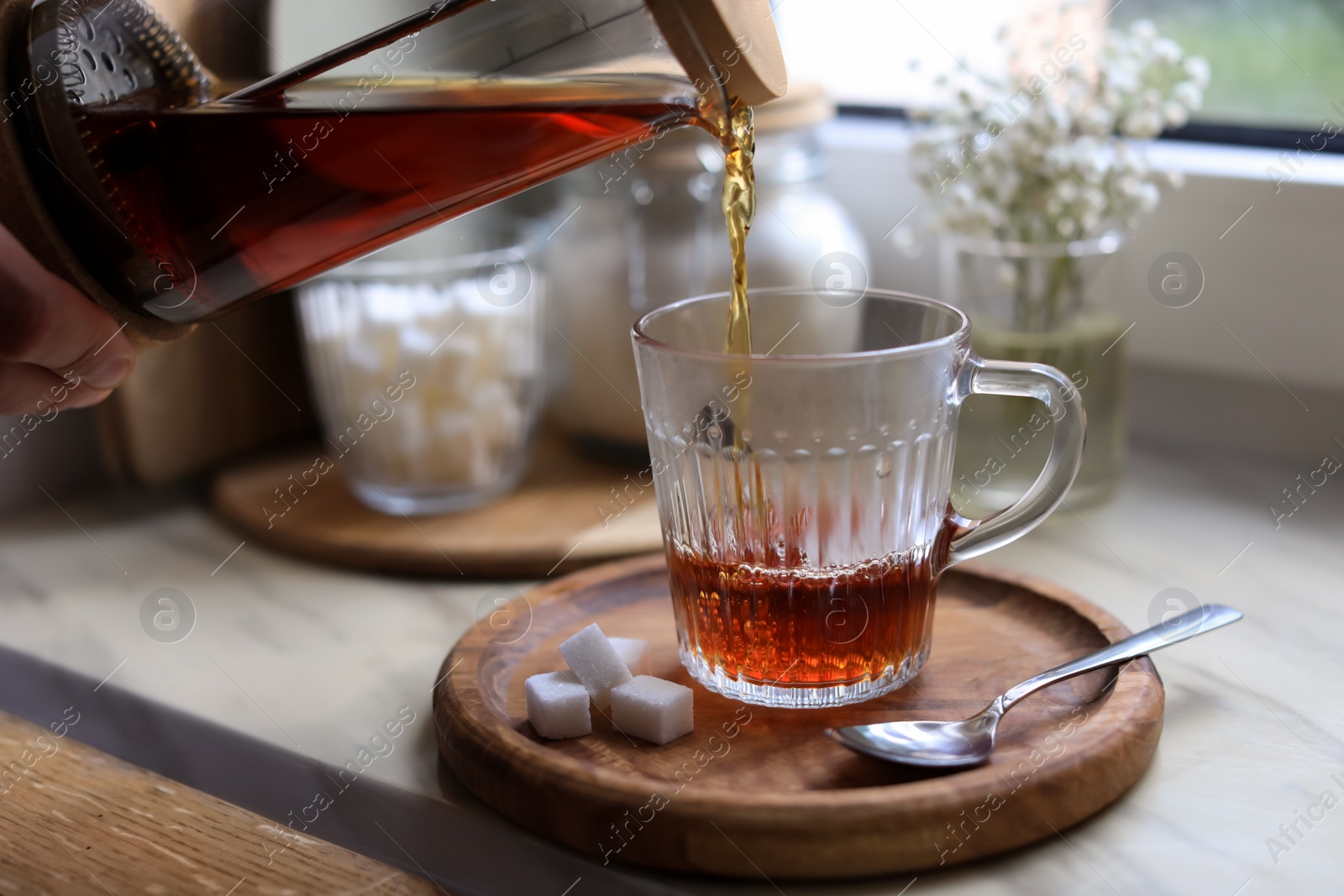 Photo of Woman pouring delicious tea into glass cup at table, closeup