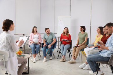 Photo of Group of pregnant women with men and doctor at courses for expectant parents indoors