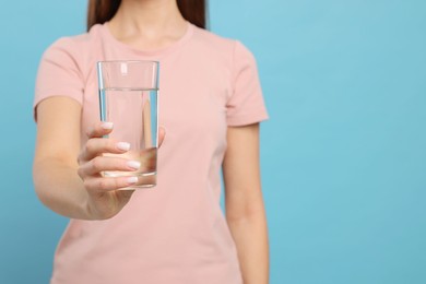 Photo of Healthy habit. Closeup of woman holding glass with fresh water on light blue background, space for text