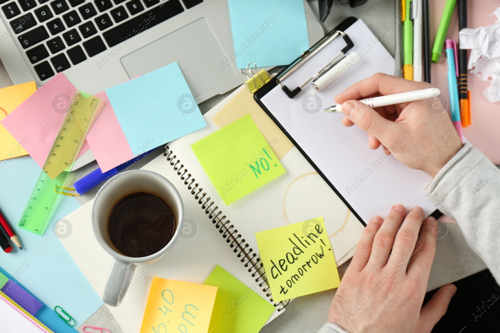 Photo of Man writing at messy table, top view. Concept of being overwhelmed by work