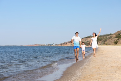 Photo of Happy family walking on sandy beach near sea, space for text. Summer holidays