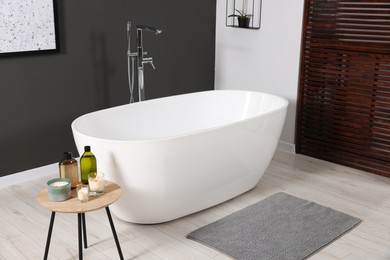 Photo of Stylish bathroom interior with ceramic tub and care products on coffee table