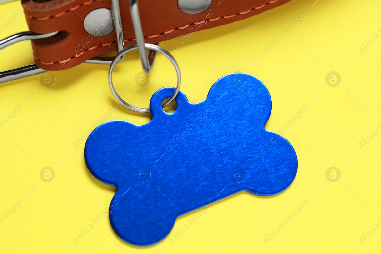 Photo of Leather dog collar with blue tag in shape of bone on yellow background, closeup. Space for text