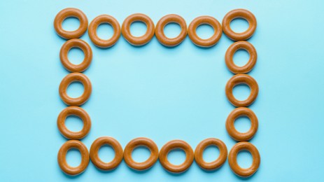Photo of Frame made of tasty dry bagels (sushki) on light blue background, flat lay. Space for text