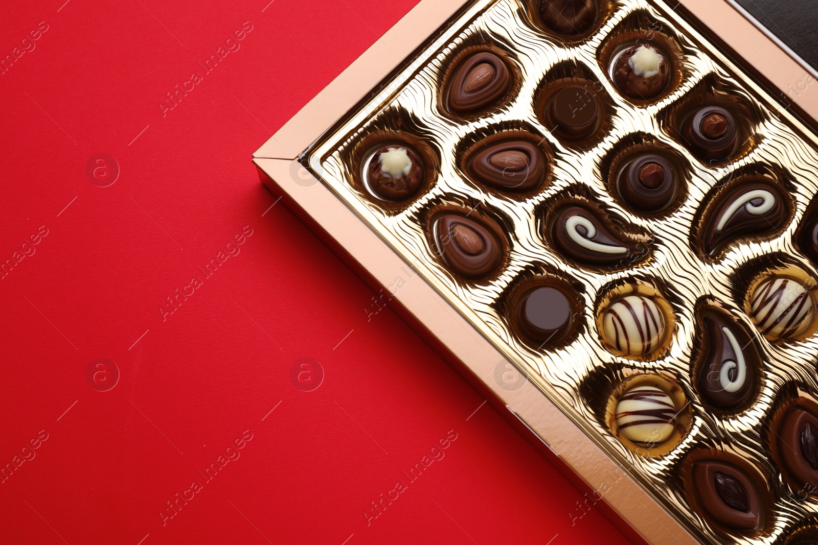 Photo of Box of delicious chocolate candies on red background, top view. Space for text