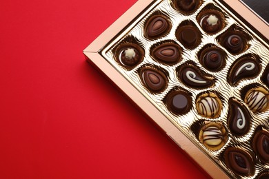 Photo of Box of delicious chocolate candies on red background, top view. Space for text