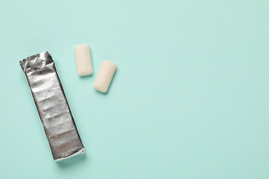 Photo of Pack and chewing gum pieces on turquoise background, flat lay. Space for text