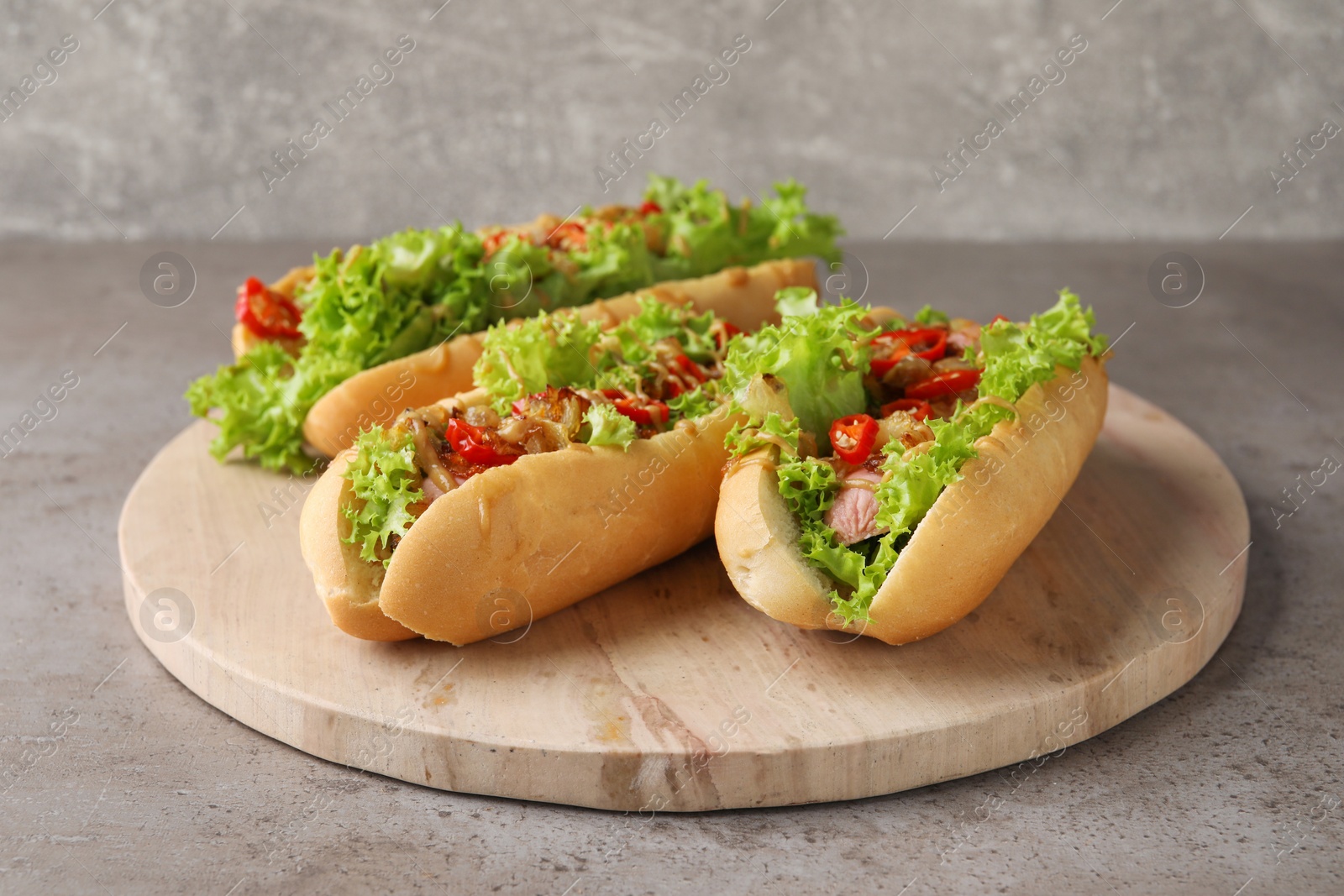 Photo of Tasty hot dogs with chili, lettuce and sauce on grey textured table, closeup