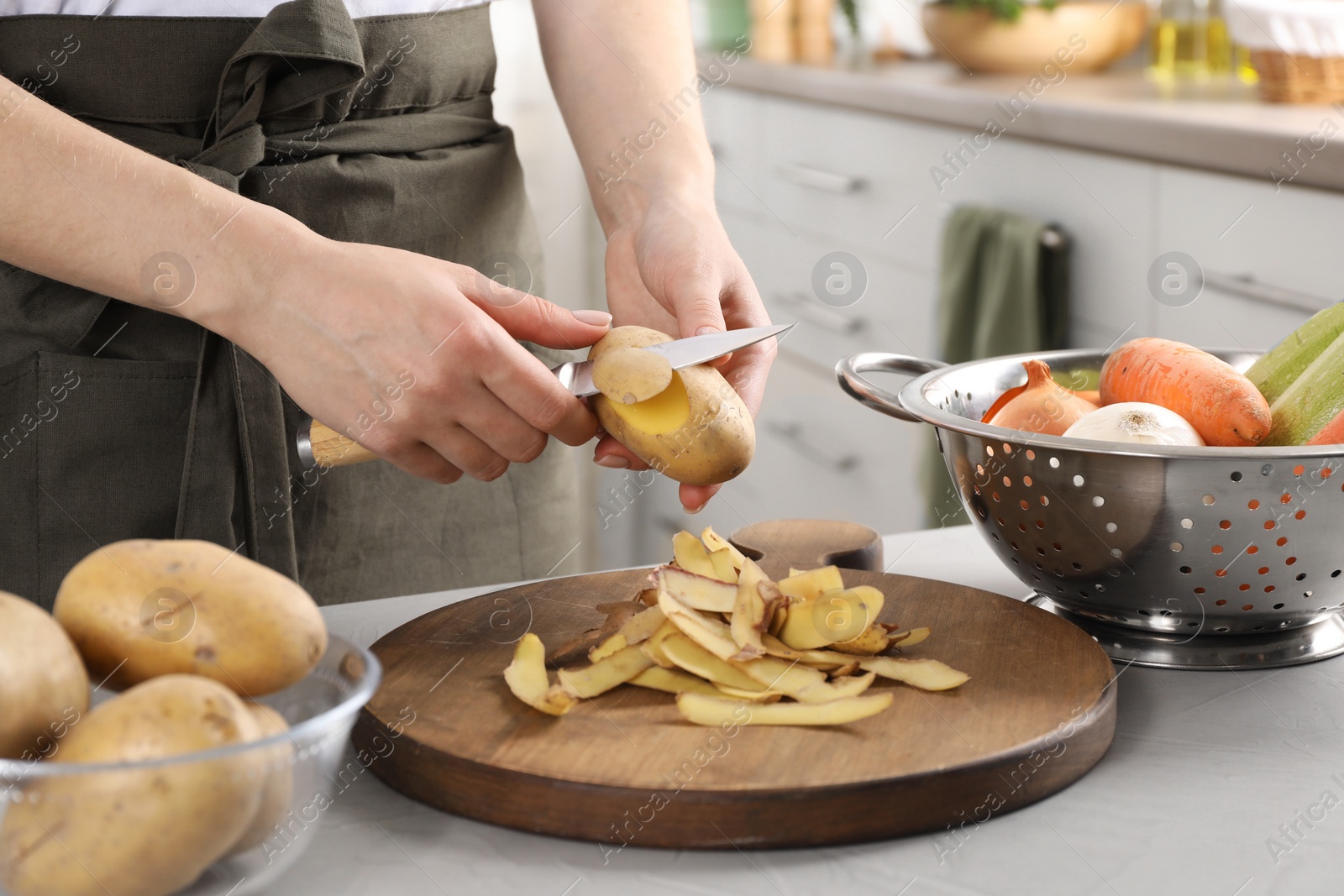 Photo of Woman peeling fresh potato with knife at light table indoors, closeup