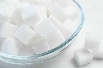 Many sugar cubes in glass bowl on white wooden table, closeup