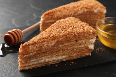 Photo of Slices of delicious layered honey cake served on black table, closeup