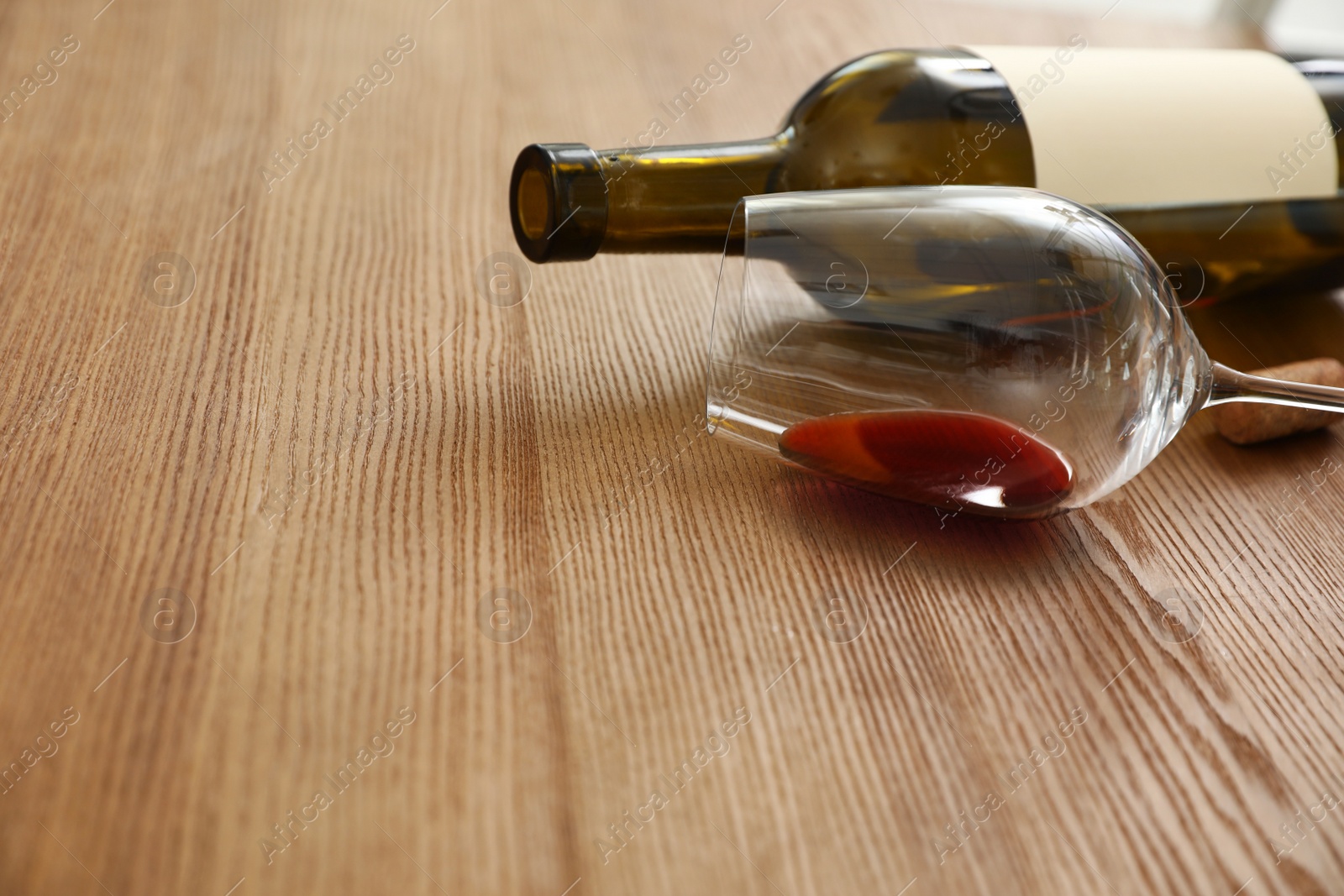 Photo of Overturned glass and bottle of wine on wooden background. Space for text