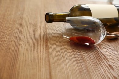 Photo of Overturned glass and bottle of wine on wooden background. Space for text