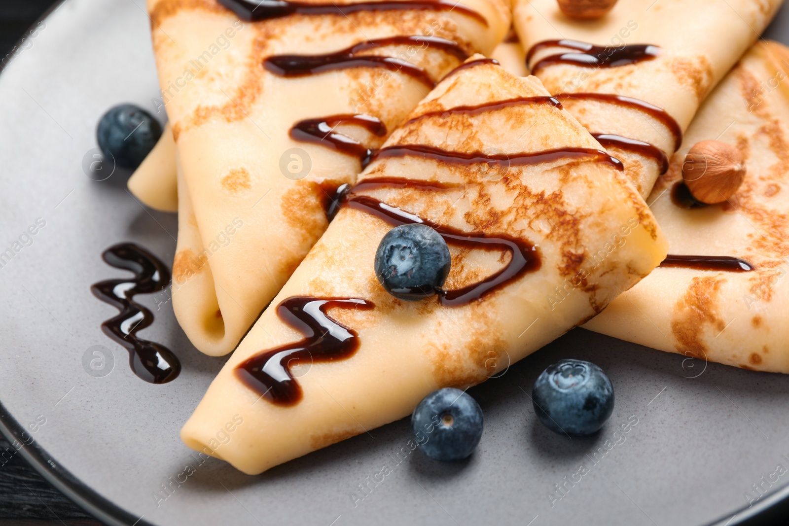 Photo of Delicious thin pancakes with chocolate, blueberries and nuts on plate, closeup