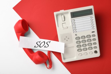 Image of Telephone and paper note with abbreviation SOS on color background, flat lay. Emergency call