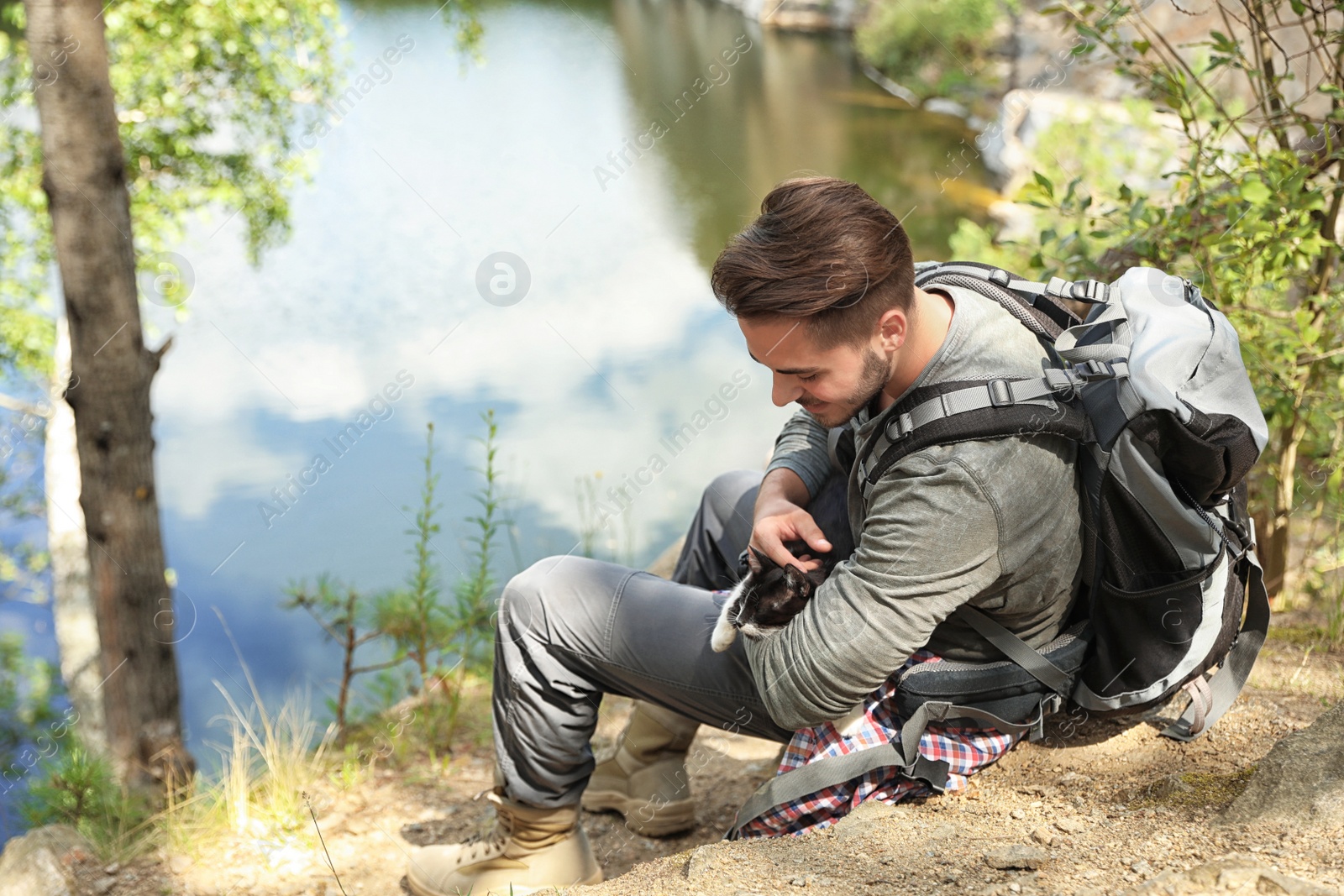 Photo of Young man with cute cat near lake. Camping season