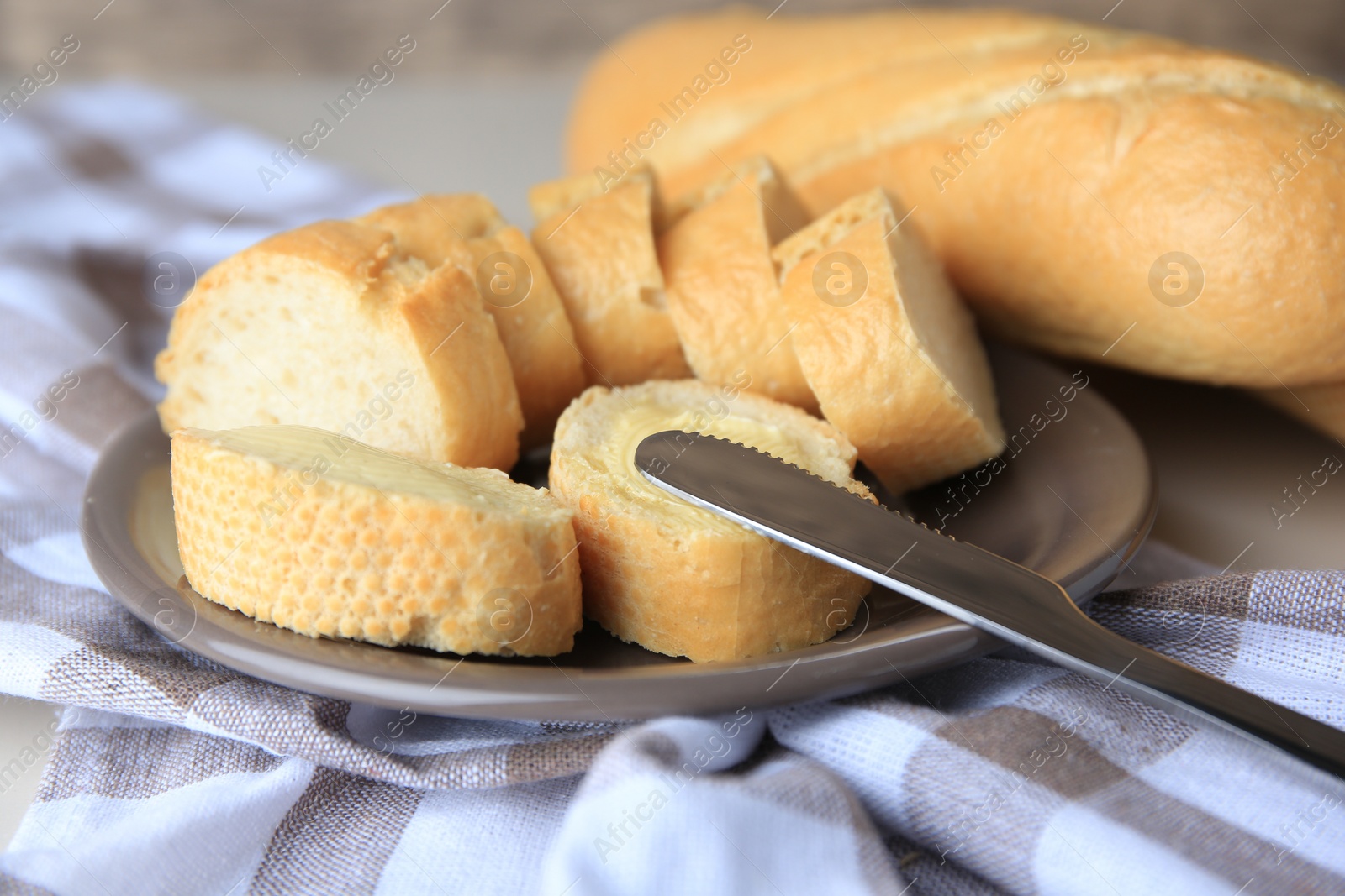 Photo of Whole and cut baguettes with fresh butter on checkered tablecloth, closeup