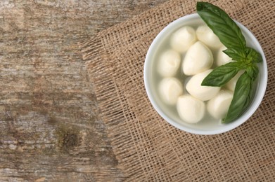 Tasty mozzarella balls and basil leaves in bowl on wooden table, top view. Space for text