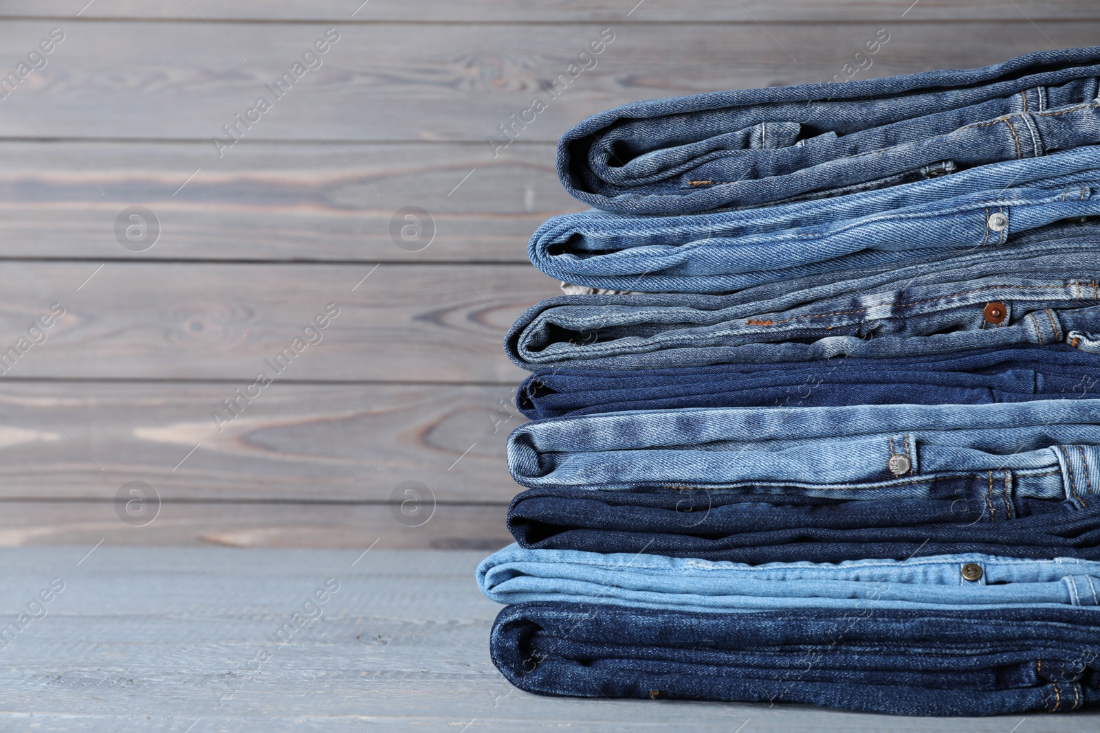 Photo of Stack of different jeans on grey wooden table. Space for text