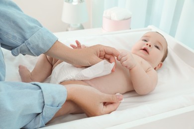 Mother changing baby's diaper at home, focus on hands