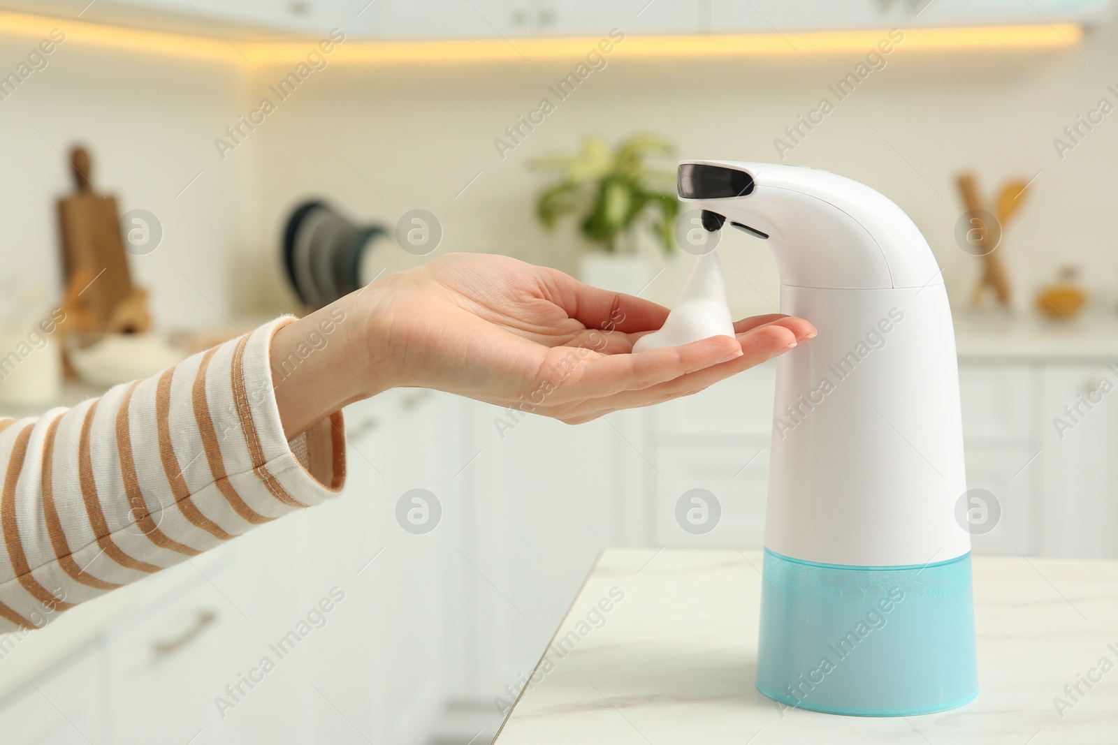 Photo of Woman using automatic soap dispenser in kitchen, closeup