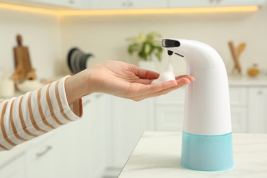 Woman using automatic soap dispenser in kitchen, closeup
