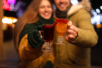 Photo of Happy couple with mulled wine at winter fair, focus on cups 