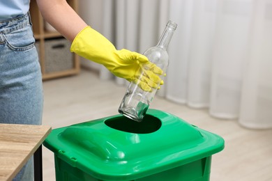 Photo of Garbage sorting. Woman throwing glass bottle into trash bin in room, closeup