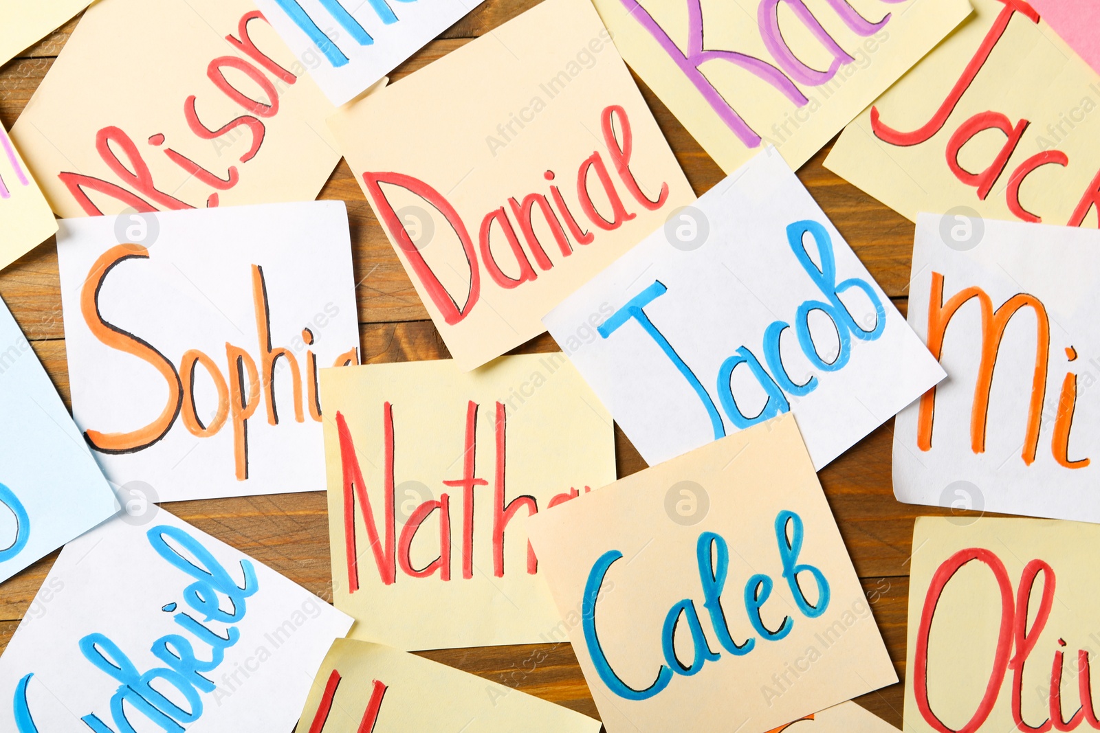 Photo of Paper notes with different baby names on wooden table, flat lay