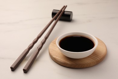 Photo of Bowl with soy sauce and chopsticks on white marble table