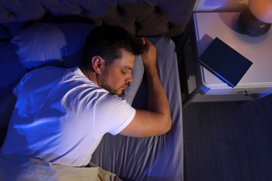 Photo of Handsome man sleeping on pillow in dark room at night, view from above. Bedtime