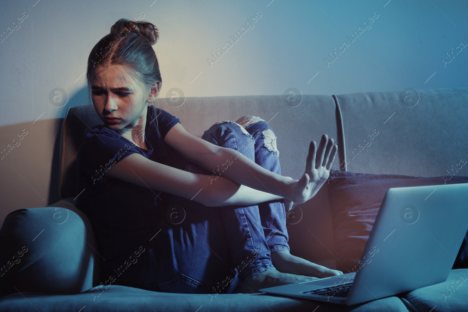 Photo of Frightened teenage girl with laptop on sofa in dark room. Danger of internet