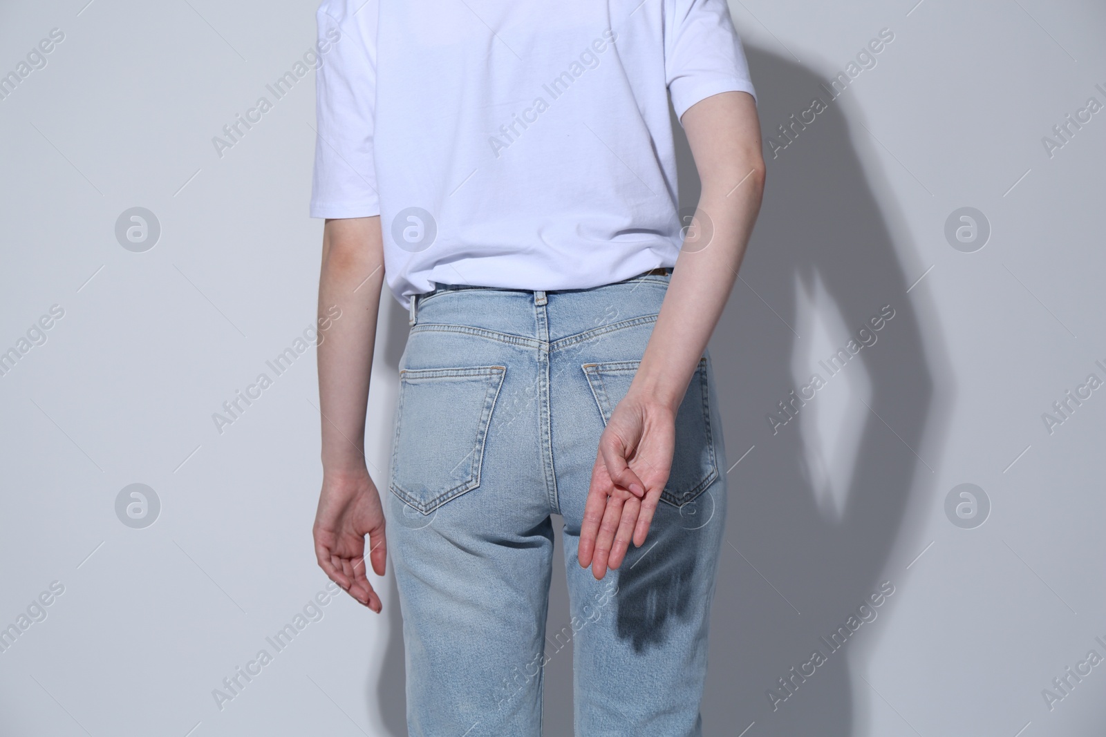 Photo of Woman showing open palm behind her back on light background, back view