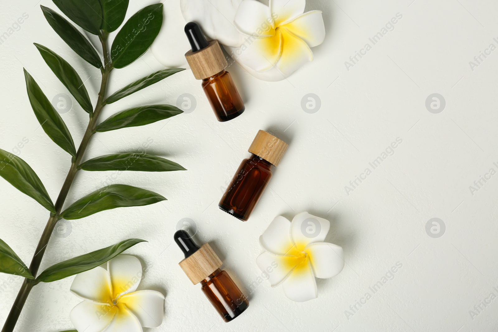 Photo of Flat lay composition with bottles of essential oil and lily flowers on white table, space for text