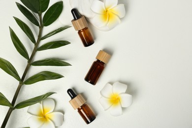 Flat lay composition with bottles of essential oil and lily flowers on white table, space for text