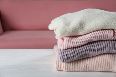 Photo of Stack of knitted sweaters on white wooden table, closeup. Space for text