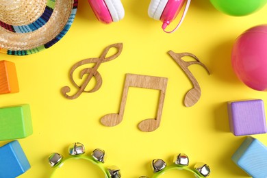 Photo of Baby song concept. Wooden notes, tambourines and toys on yellow background, flat lay
