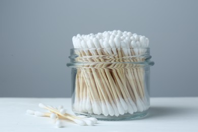 Many cotton buds on white wooden table against grey background