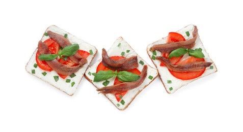 Delicious sandwiches with cream cheese, anchovies, tomatoes and basil on white background, top view