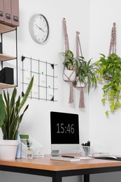 Photo of Cozy workplace with computer, modern furniture and houseplants at home