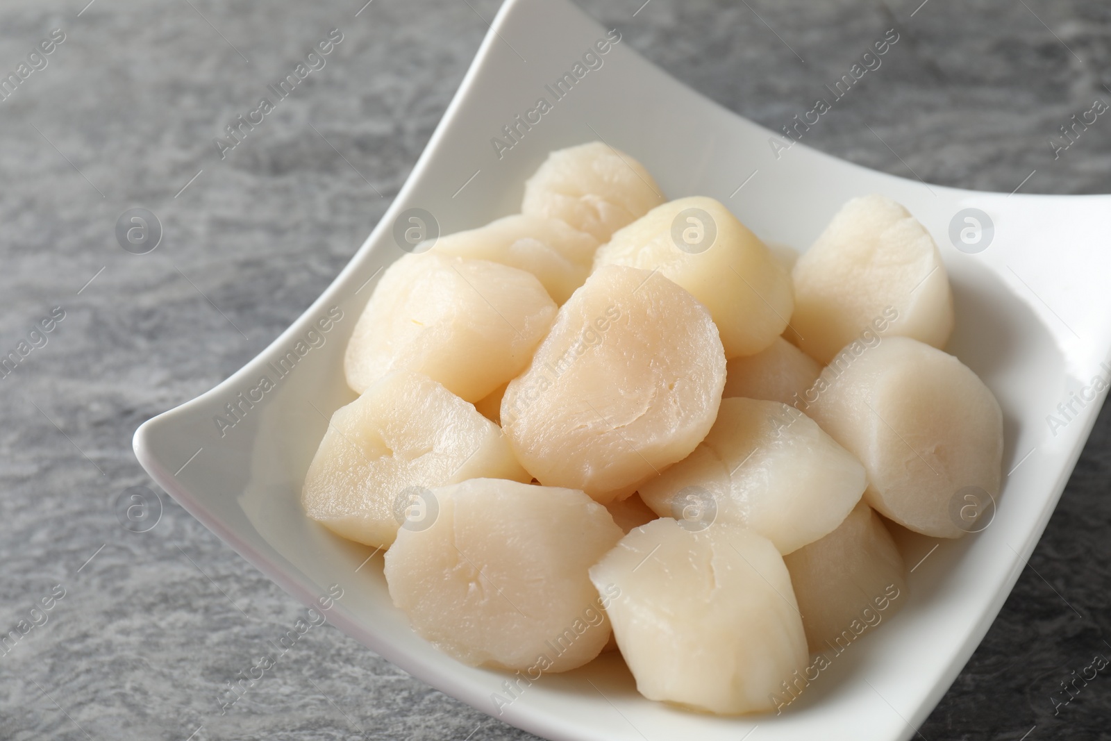 Photo of Fresh raw scallops in bowl on grey table, closeup