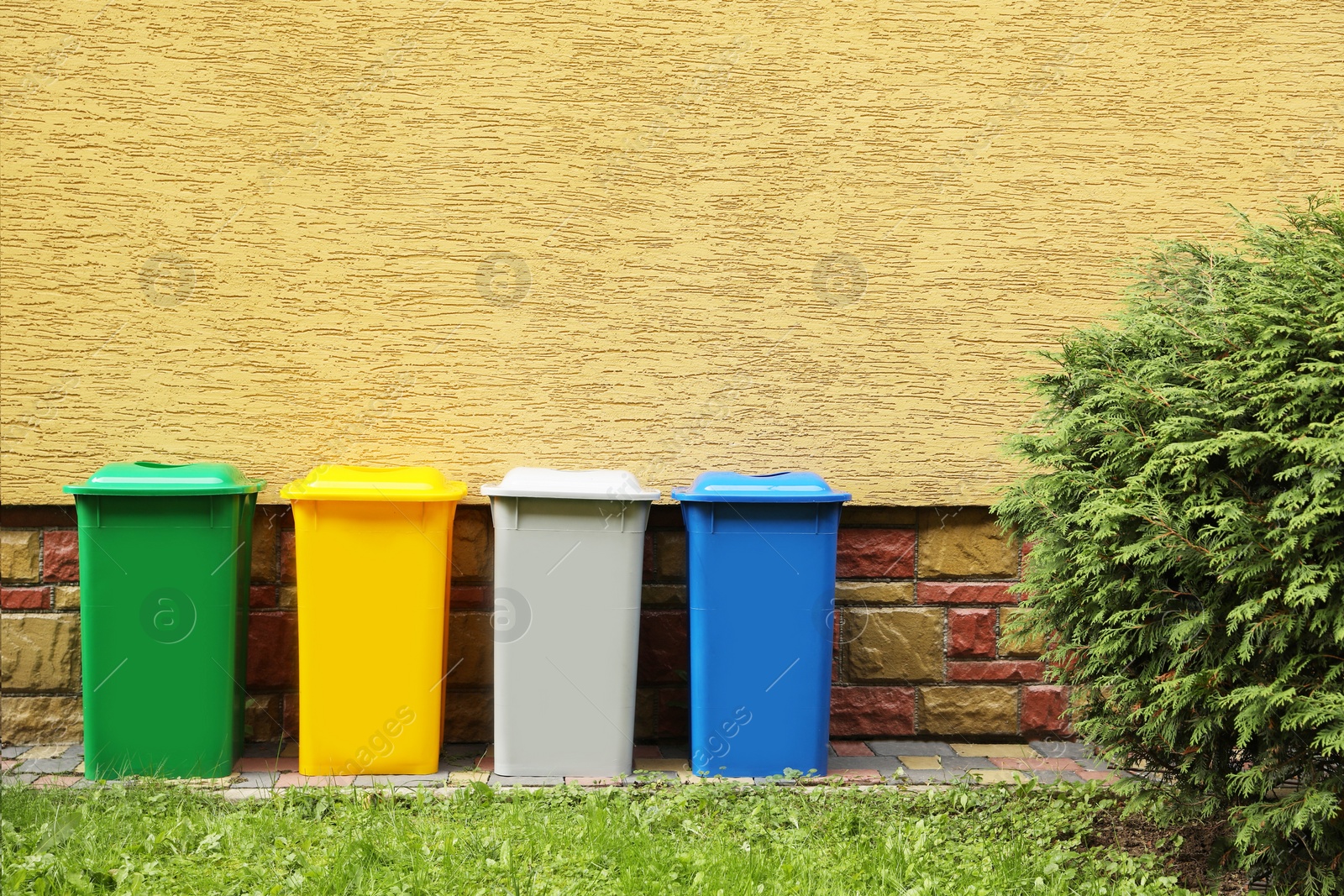 Photo of Many colorful recycling bins near yellow wall outdoors