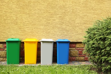 Many colorful recycling bins near yellow wall outdoors