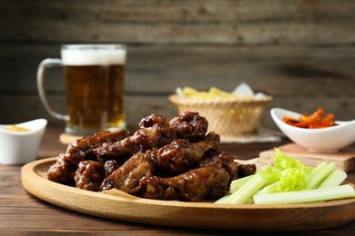 Photo of Delicious chicken wings served with beer on wooden table, closeup