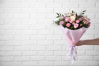 Photo of Woman with bouquet of beautiful roses near white brick wall, closeup. Space for text