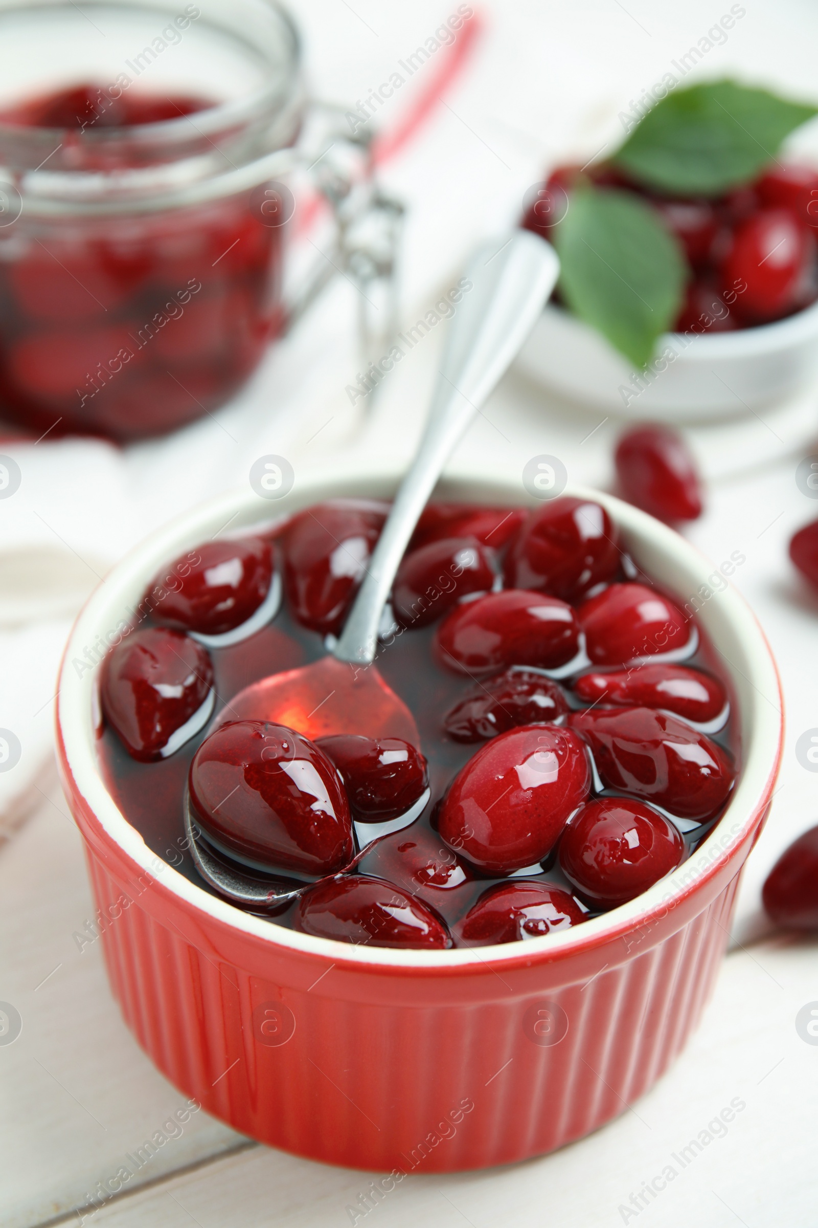 Photo of Delicious dogwood jam with berries and spoon on white wooden table, closeup