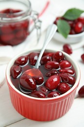 Photo of Delicious dogwood jam with berries and spoon on white wooden table, closeup